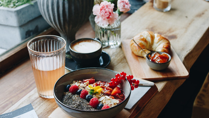 Eine Bowl mit Porridge und Obstkompott, ein Croissant mit hausgemachter Marmelade, Cappuccino und eine Rhabarberschorle