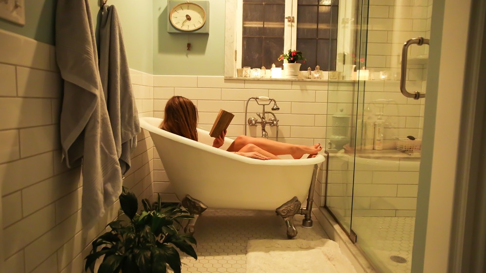 Eine Frau liegt in einer kleinen Badewanne und liest ein Buch