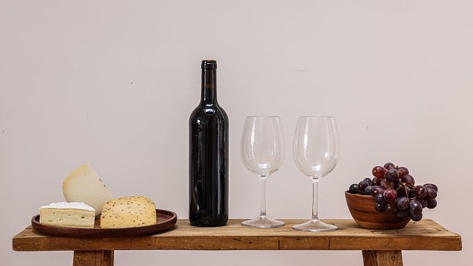 Holztisch mit kleiner Käseauswahl, Weinflasche und Gläsern